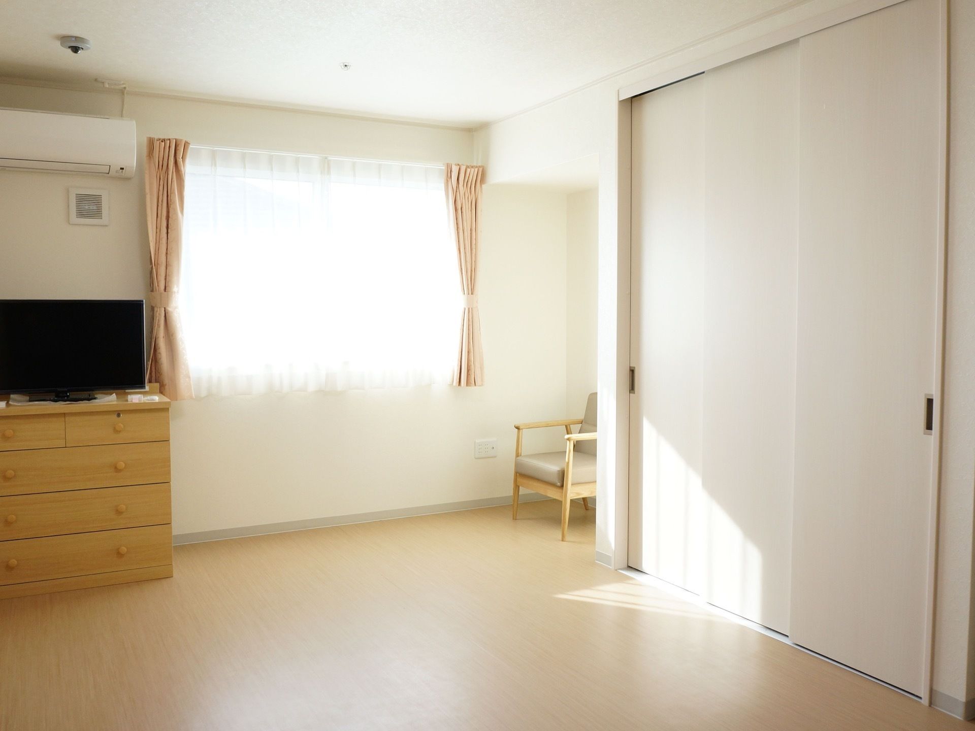 日当たりの良いフローリングの居室。壁にはエアコンが取り付けられている。チェストやテレビが設置されている。
