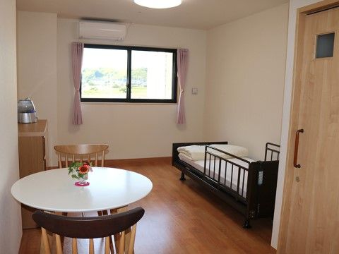 窓にピンクのカーテンが掛かり、テーブルには花が飾られた部屋。家具の色が部屋の色とコーディネートされており、落ち着ける雰囲気の居室である。