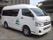 車椅子のマークが付いた白いワゴン車が停まっている。後ろのドアは左側についている。車体には施設名や、木の絵が描かれている。