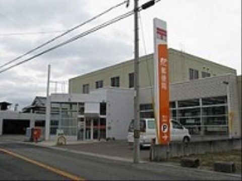 施設の近くにある郵便局の外観である。縦長の郵便局の看板や、赤いポストが見える。建物の前には駐車スペースがある。