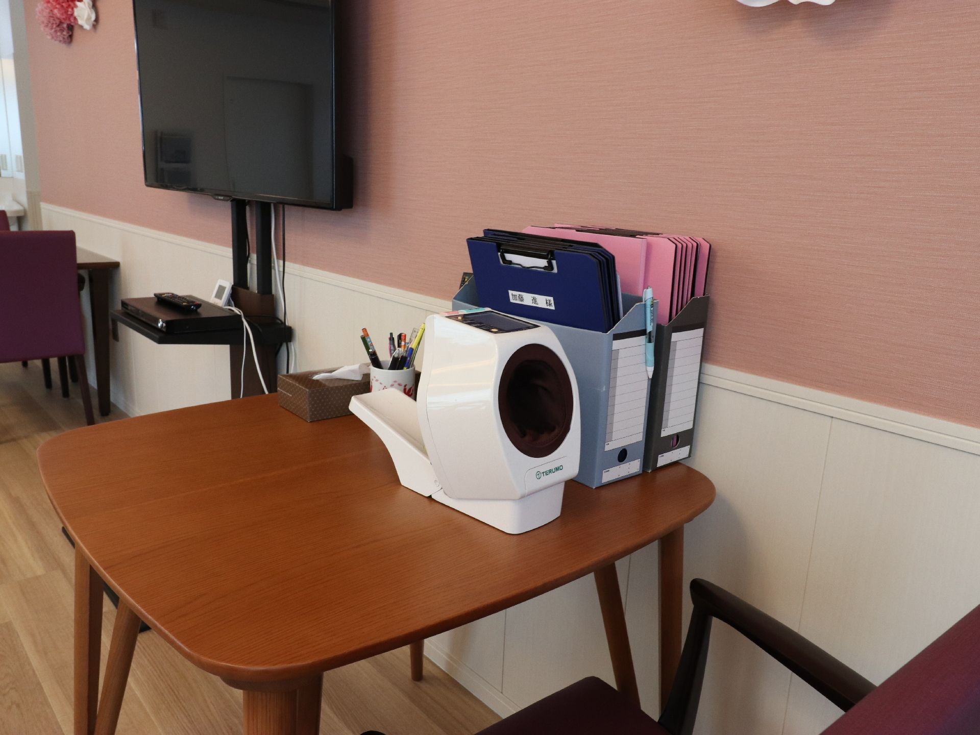 自動で血圧を測定することができる機械が、茶色のテーブル上に置いてある。すぐ横には、ファイルボックスが2個並んでいる。