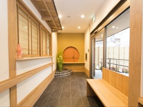 床に黒いタイルが敷かれている。黄色い花が花壇に植えられている。木製のベンチも設置されている。外には緑が植えられている。