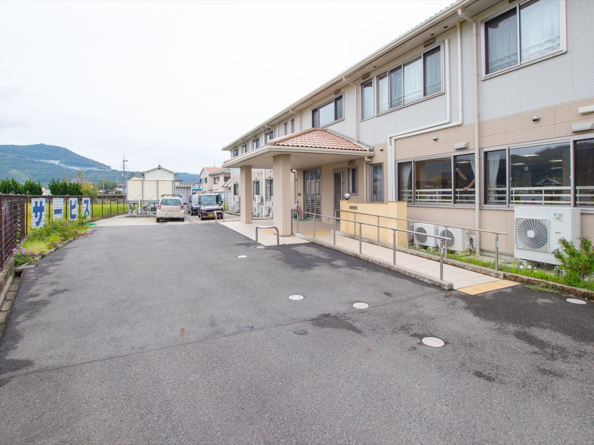 施設の敷地内はアスファルトで舗装されている。玄関前のスペースには屋根がついており、そのすぐ前まで車を寄せることができる。