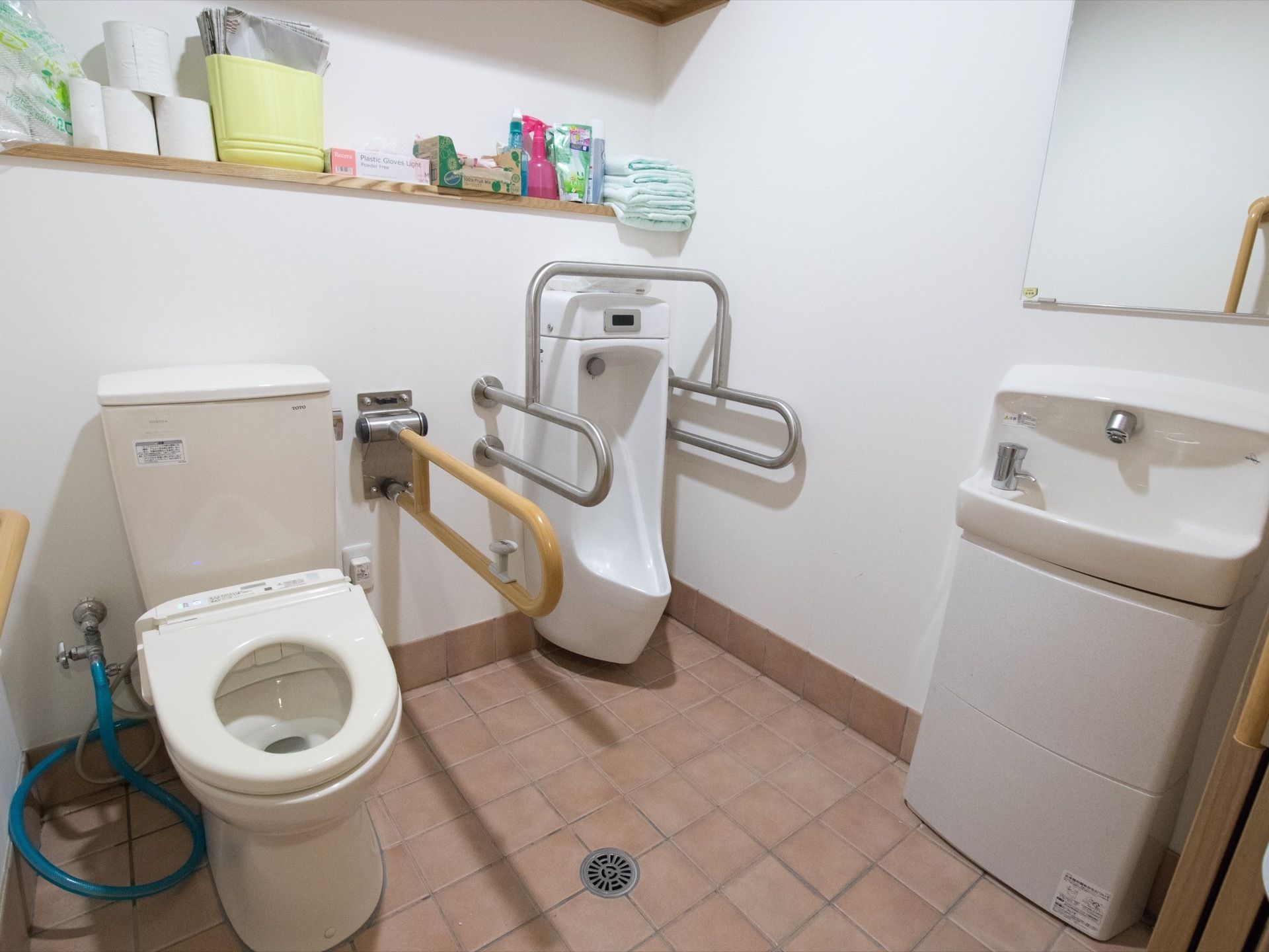 共用のトイレには小便器もあり、手すり付きのセンサー式水洗タイプになっている。手前には鏡付きの手洗い器が設置されている。