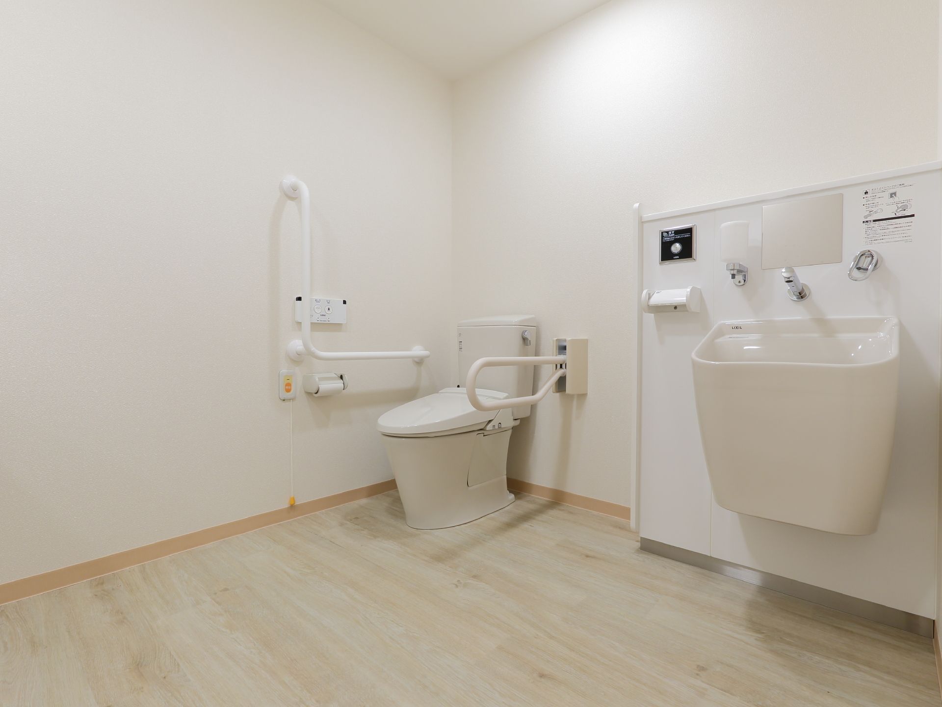 白基調のトイレで、洗面台が一緒になっている。手すり、ナースコールがあり、広いので車椅子のまま入れる。