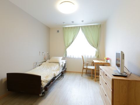 白いベッドとナチュラルウッドの家具が置かれている居室