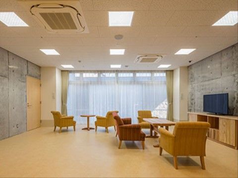 黄土色と茶色のファブリックを使ったソファーが、通路を残して配置されている。壁側の中央にテレビを置き、入居者様同士で鑑賞することができる。