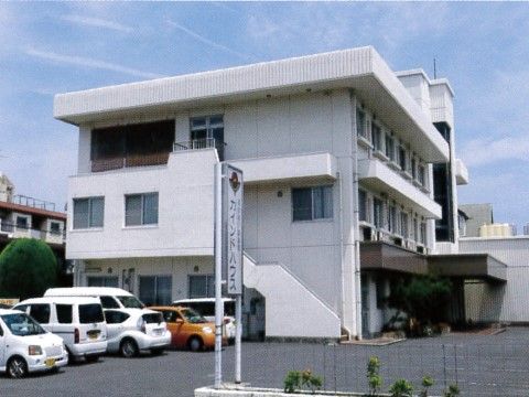 白い３階建てのグループホームである。敷地内にはアスファルトで舗装された充分な駐車スペースを確保している。
