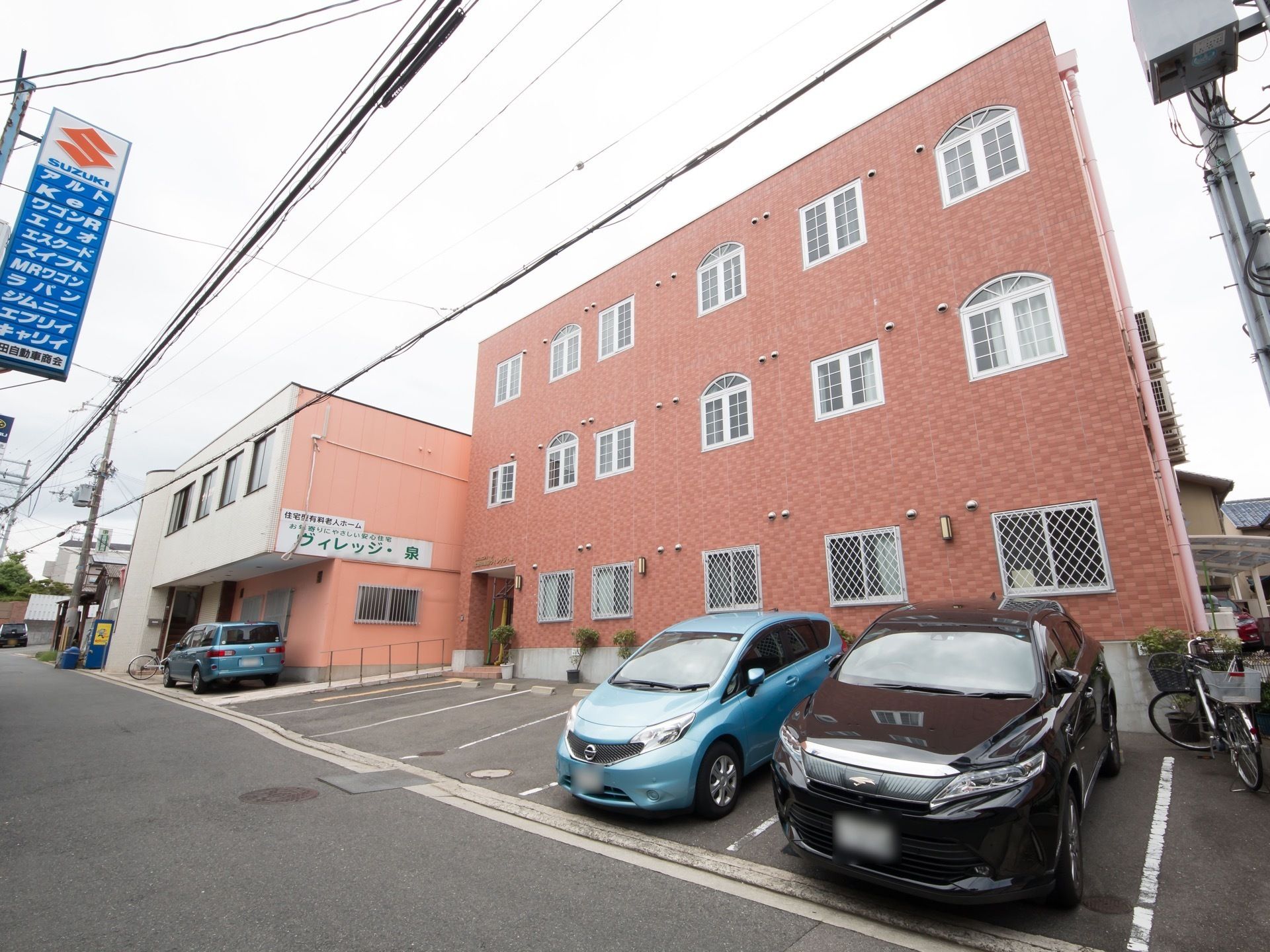 道路から見上げた施設建物本体。各居室などにつながるエアコン用の室外機が側面の一か所に集中して配置されている。