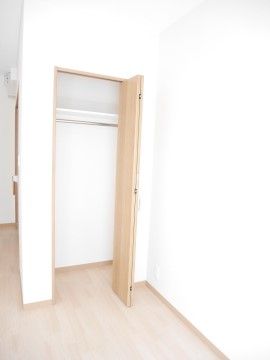 居室の白い壁に備え付けられたクローゼット。明るい木目の扉は折れ戸になっている。上部は棚があり、その下にハンガーポールが設置されている。