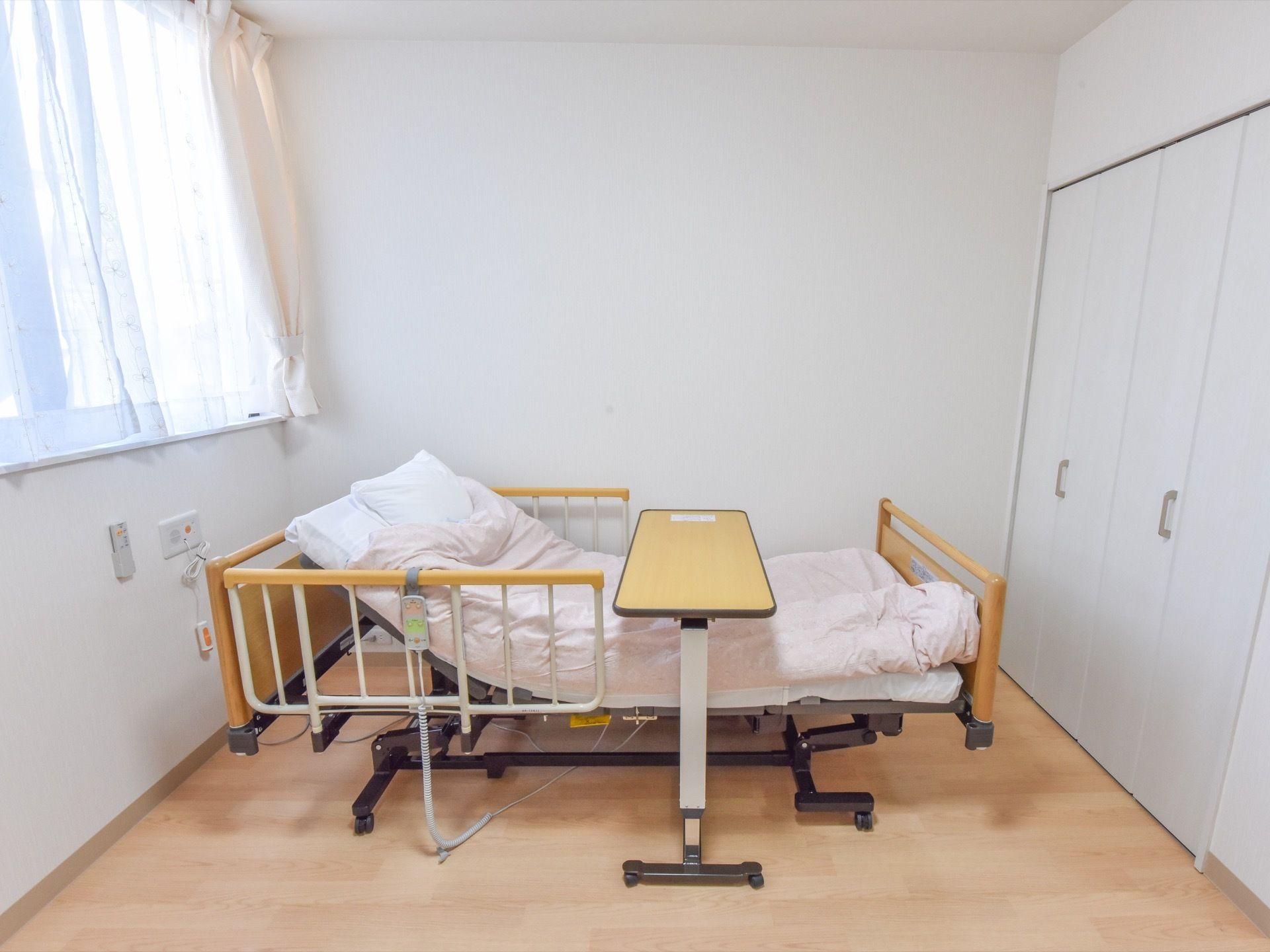 電動式ベッドの真ん中あたりに、ライトブラウンの細長いテーブルがセットされている。緊急用の呼出ボタンが、左側の壁にある。