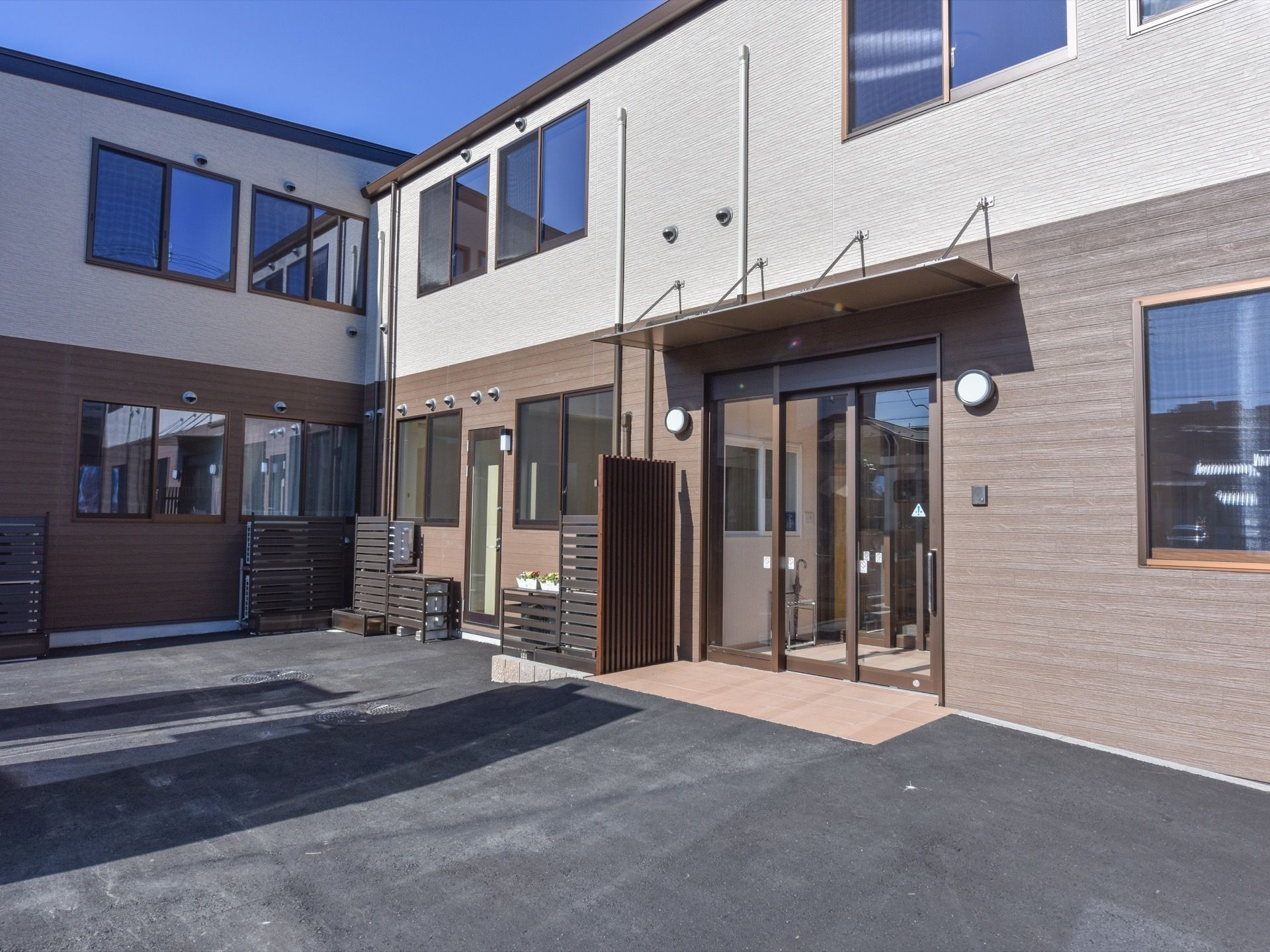 施設はシンプルな２階建てで、茶色系の外壁に落ち着きを感じる建物である。出入口には段差もなくスムーズな出入りが可能になっている。