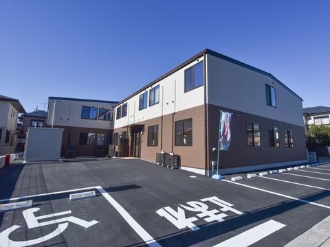 広い駐車場と、白色と茶色の外壁があるグループホーム
