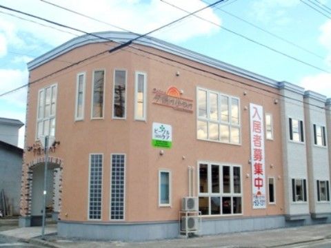 薄い茶色の外壁があり、入居者募集中の看板がある介護施設