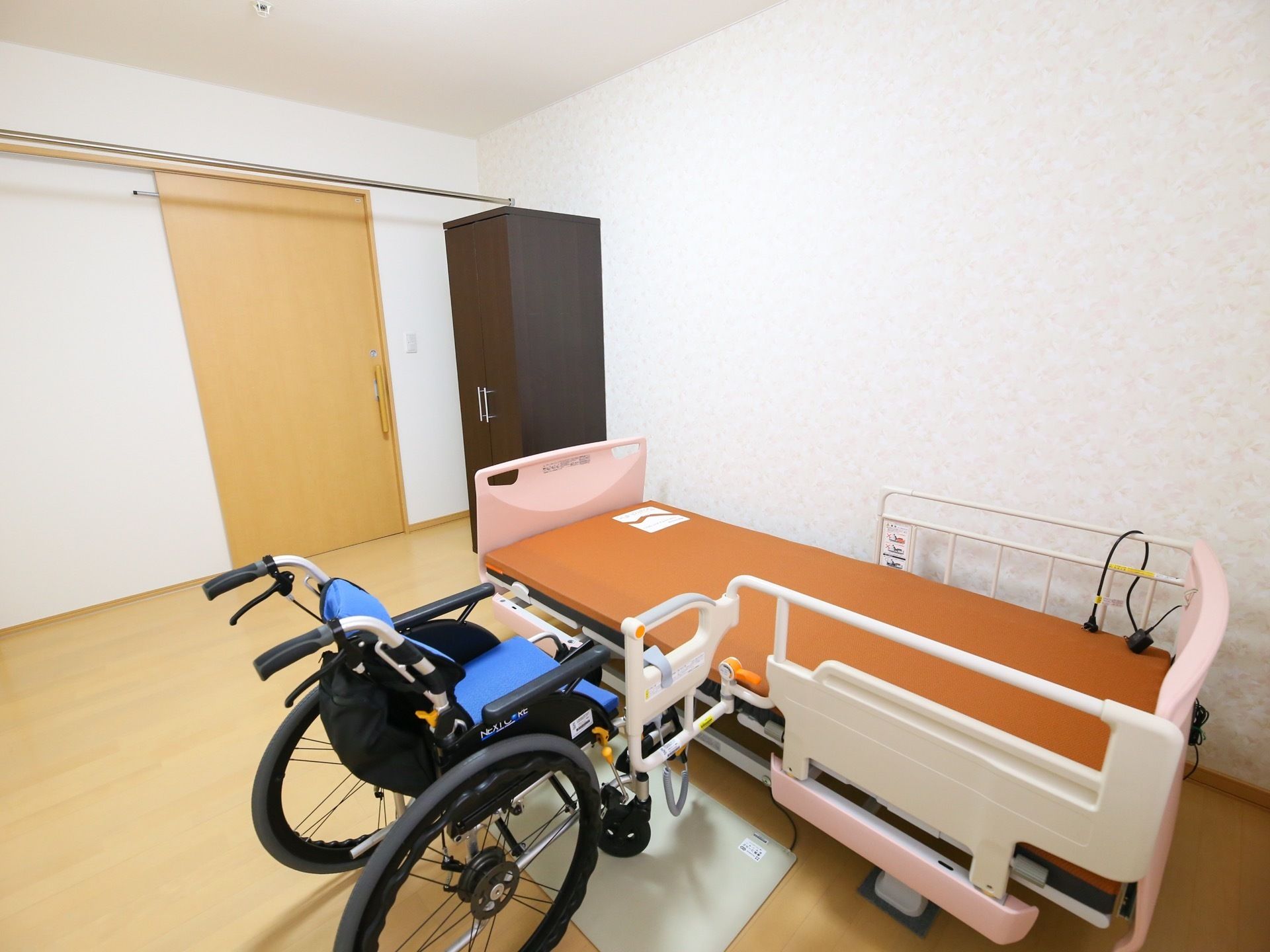 個室の居室には、介護ベッドやクローゼット、ナースコールが完備されている。車椅子が置かれた床には、フットヒーターが設置されている。