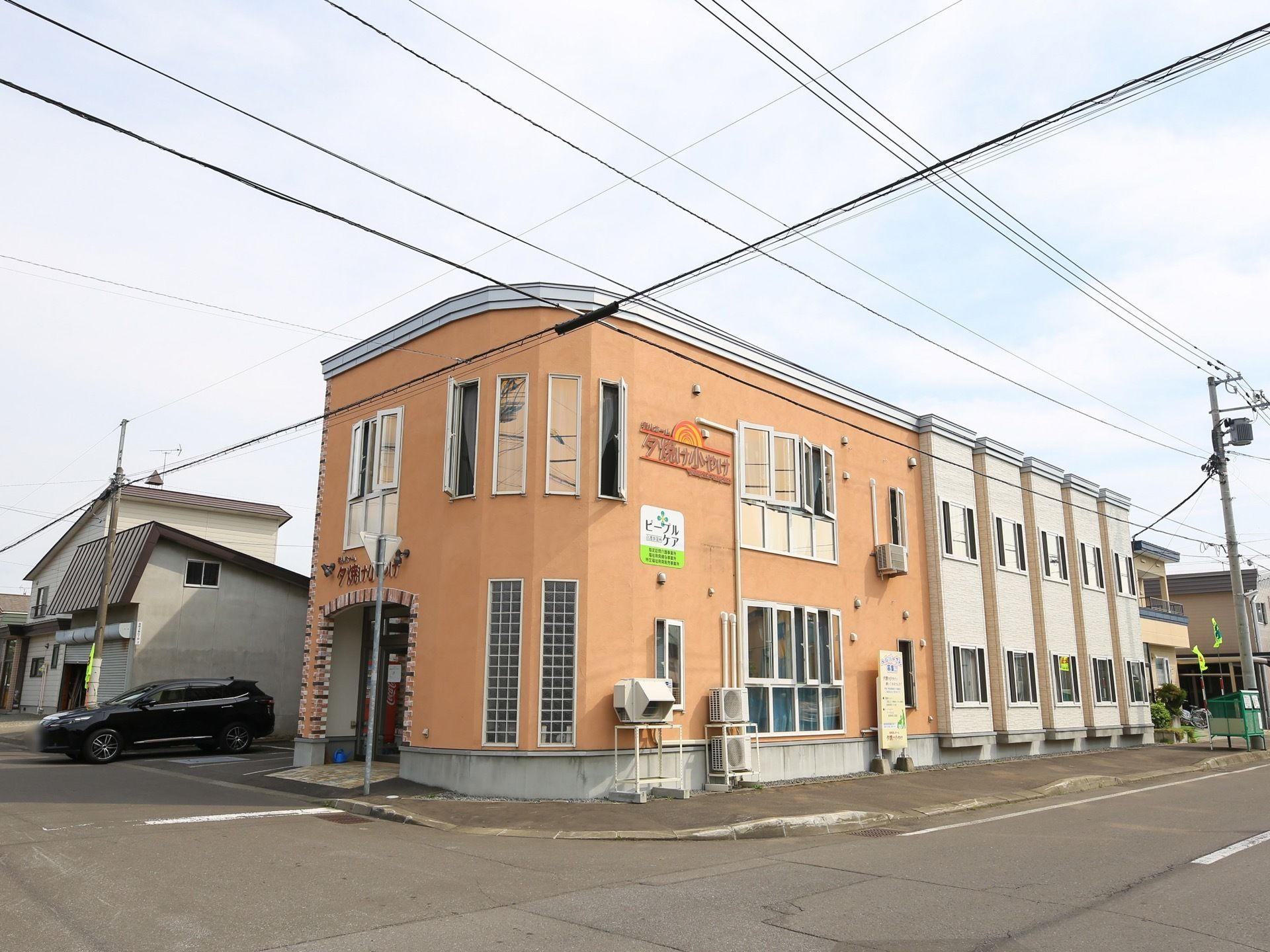 施設は２階建ての建物である。建物の壁面に複数の窓が設けられており、施設名が大きく記されている。エントランス横に駐車場がある。