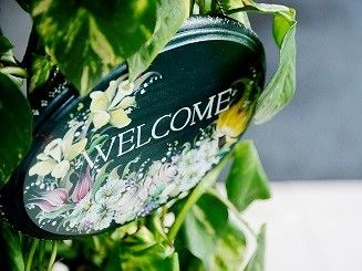 緑の観葉植物に囲まれ、welcomeの文字と花々のイラストの入った丸いプレート看板
