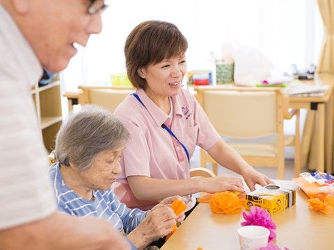 色紙で花飾りを作っている高齢者と、女性の介護スタッフ
