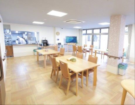 奥に厨房が併設された食堂である。複数の４人掛けダイニングテーブルが配置されている。壁や柱には、手すりが備わっている。