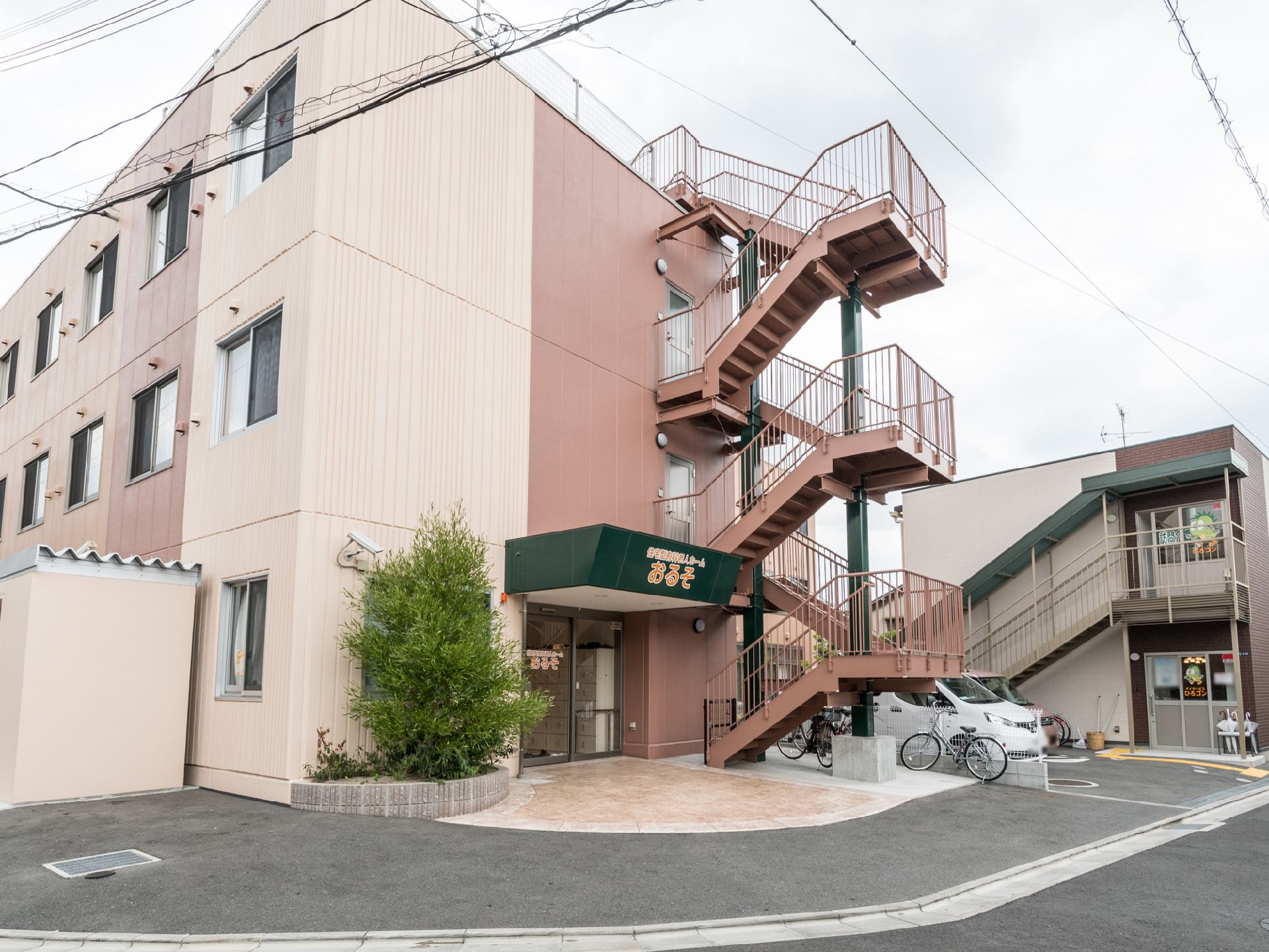 施設は３階建ての建物である。建物横に駐車場と駐輪スペースが設けられている。各階から出られる外階段が設置されている。