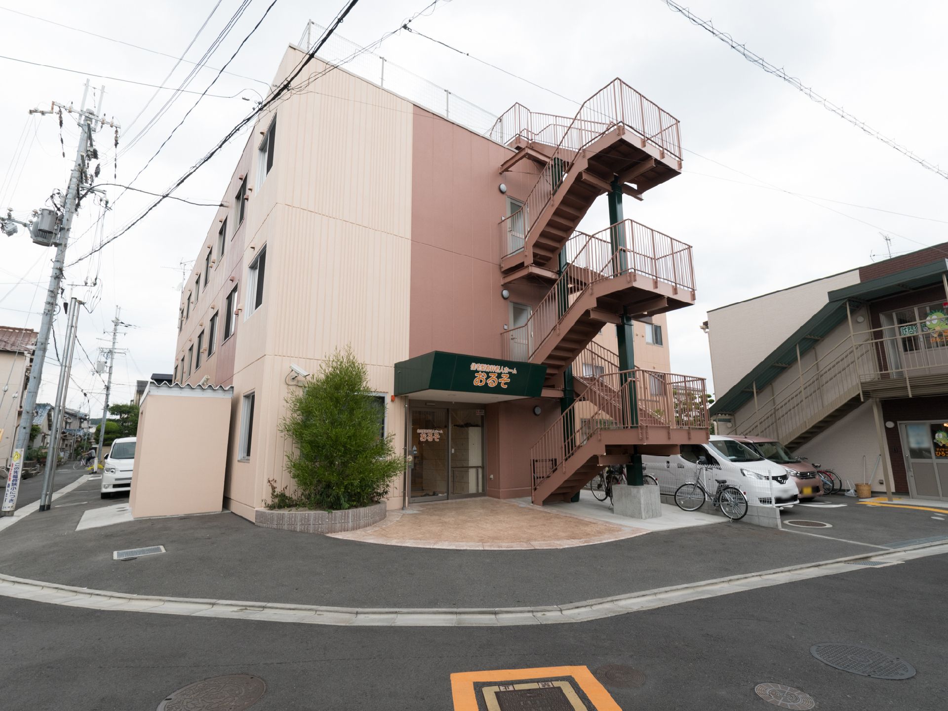 施設は３階建で屋上があり、非常階段が備わっている。玄関アプローチには、庇が付いている。建物の両サイドには、駐車スペースがある。