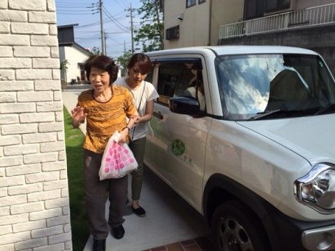白いミニバンと白い壁の間を歩くおばあさんと若い女性