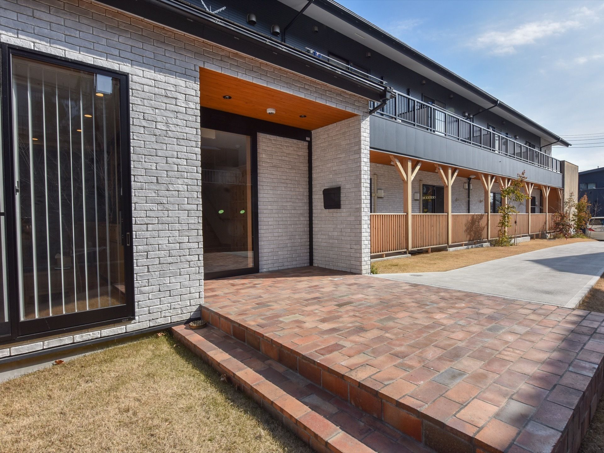 木造２階建ての施設である。１階に木製のフェンスを設置し、建物の横側に通路を設けている。玄関ドア前の地面はレンガ調になっている。