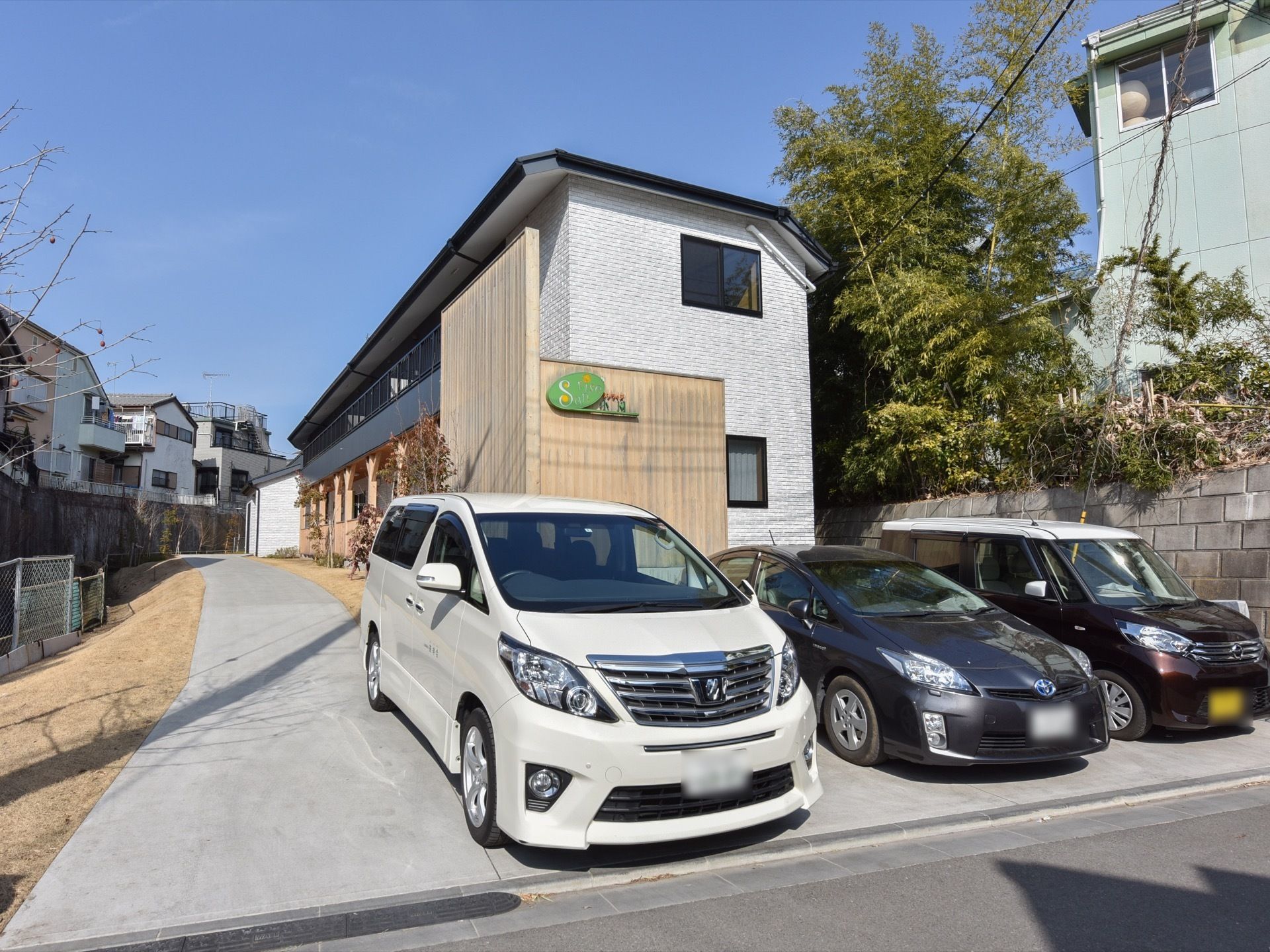 道路に面した敷地内には車を停められるスペースがある。玄関に繋がるコンクリート作りの通路があり、両側に芝生を敷いている。