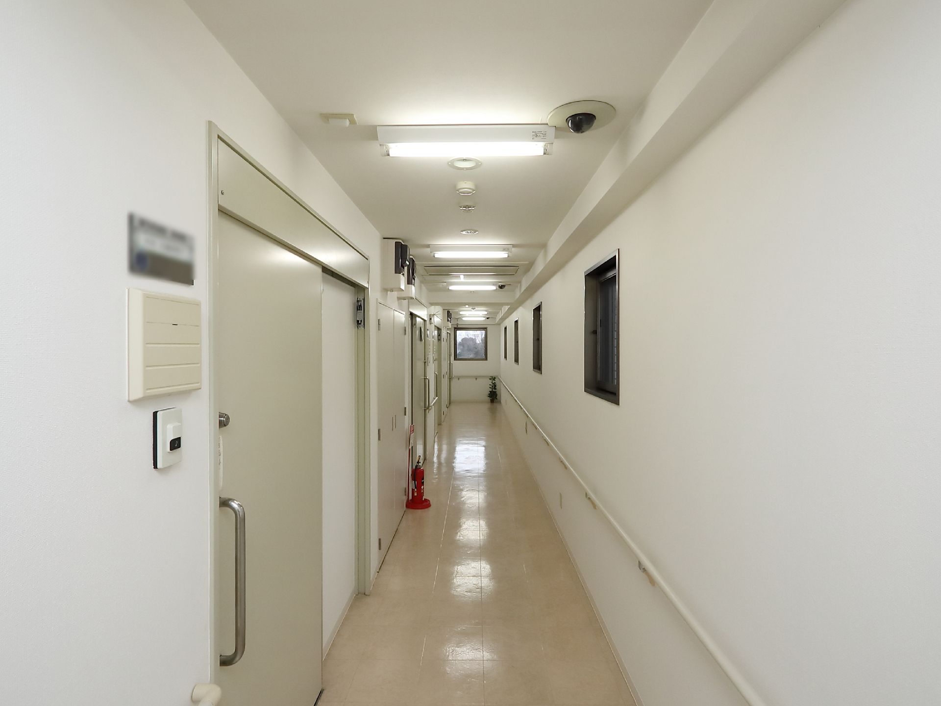 細長の通路が真っ直ぐに伸びている。片側の壁沿いに手すりが設置されている。廊下に沿って並ぶ部屋のドアは、スライド式になっている。