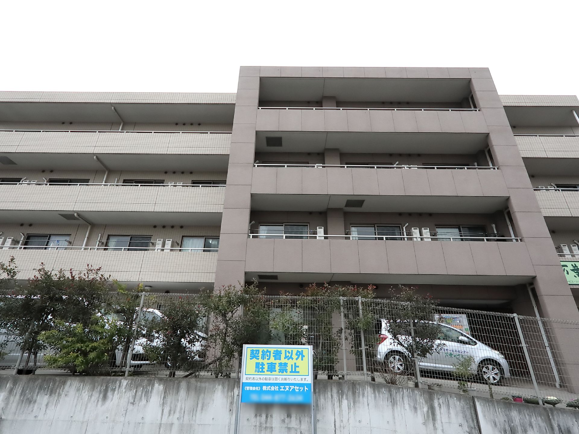 淡い色の外壁の鉄筋コンクリート造りの施設である。各階にベランダが設置されている。建物の前に駐車場が設けられている。