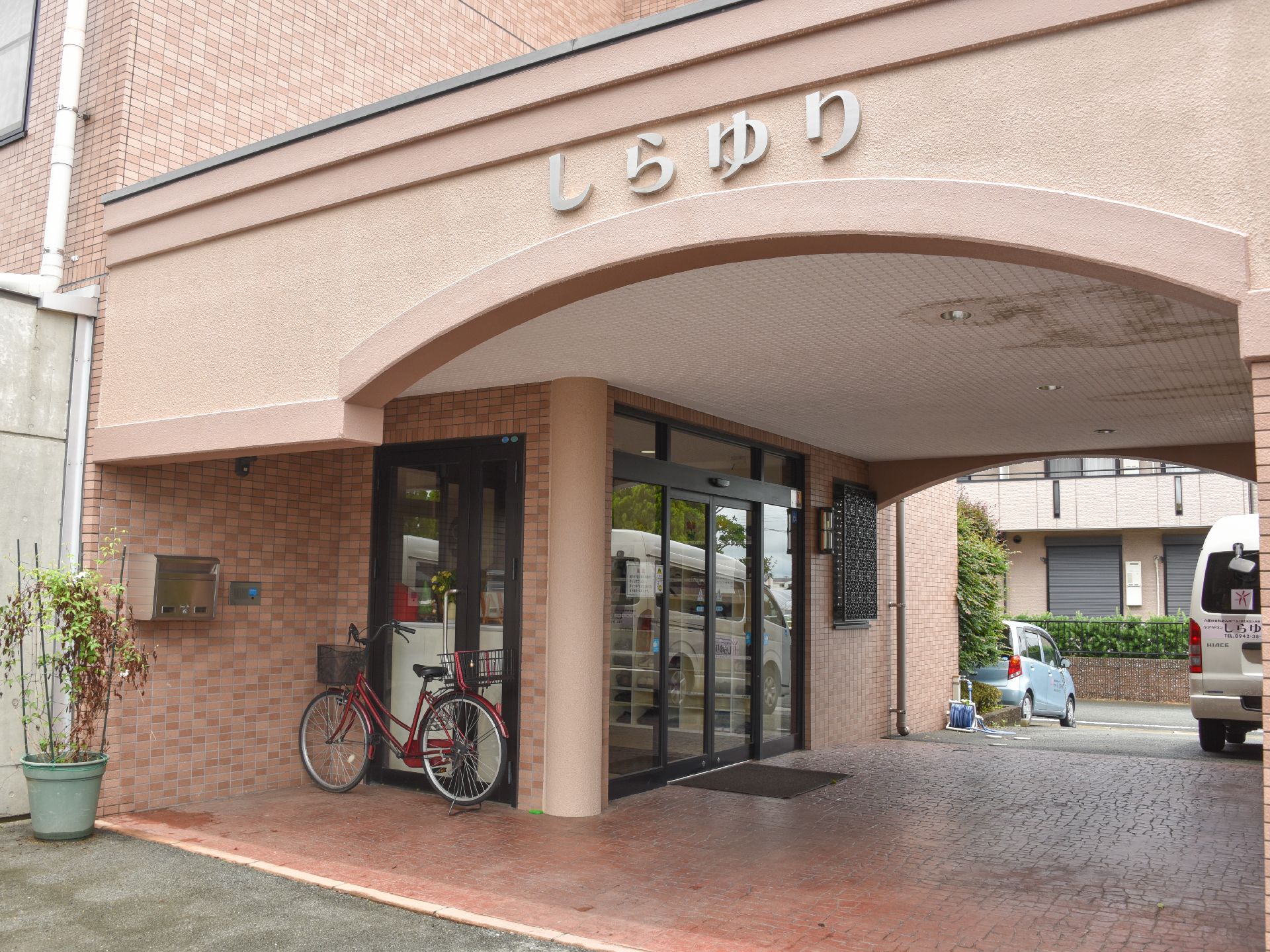 車両から昇降する施設入口は屋根付きで、雨の日でも快適に通所できる。通路は送迎車が停まっても左右に十分幅の余裕がある。