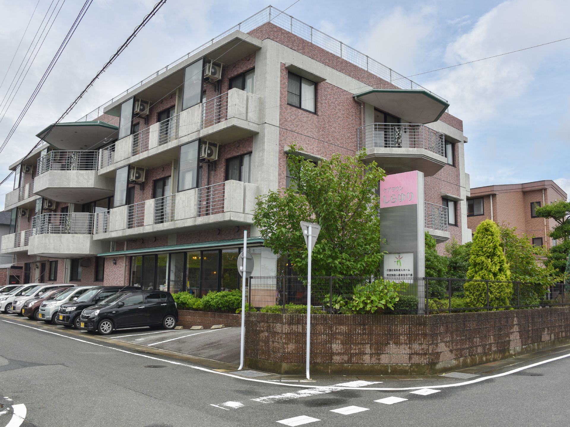 閑静な住宅街にあり、穏やかなピンクのレンガ風の外観に植木の緑が映える。日当たりのよい角地で施設看板もわかりやすい。