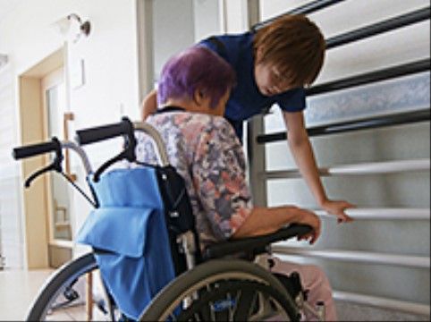 青い車いすに乗っているおばあさんと、茶髪の男性職員