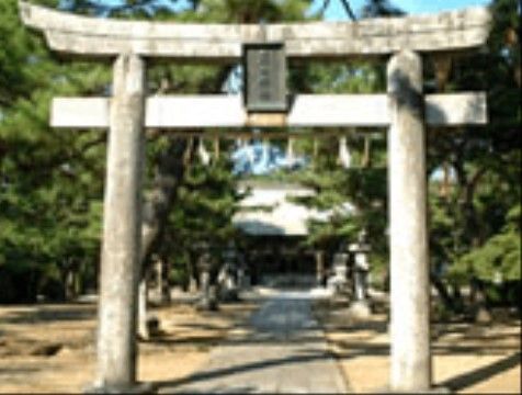 神社正面から撮られた写真である。大きな鳥居で、上部分に表札が取り付けられている。石畳の道の両サイドには木々が広がっている。