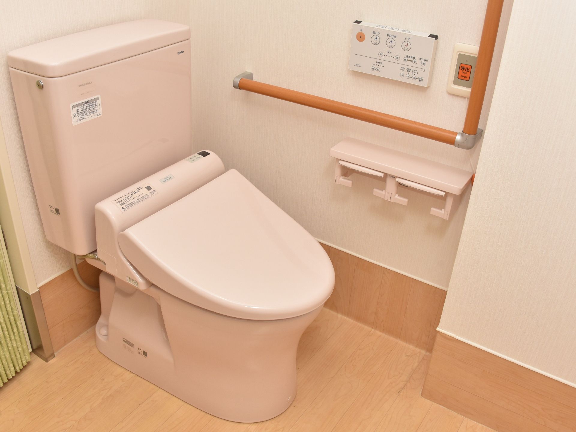 エル字型の手すりが設置している。ウォシュレット付きトイレ。ヘルプコールボタンも設置している。白を基調とした清潔感あるトイレ。