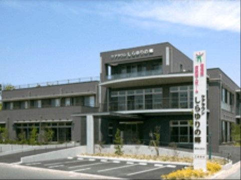 落ち着いた色合いの３階建てのグループホーム。駐車場を施設内に設けており、施設名が書かれた看板が立っている。