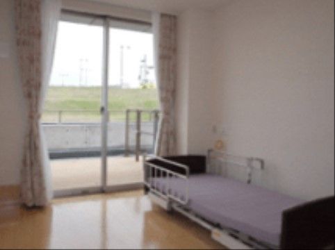 華やかなカーテンが取り付けられた居室である。介護ベッドが置かれており、大きな窓からはテラスに出られる。