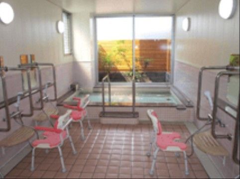 広い洗い場のある大浴場。ひじ掛けと背もたれのついたシャワーチェアが複数準備されている。窓から庭が見渡せる。