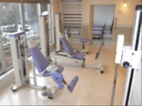 木のぬくもりが感じられる明るい空間である。窓沿いにレッグプレスなどのトレーニング機器が置かれている。