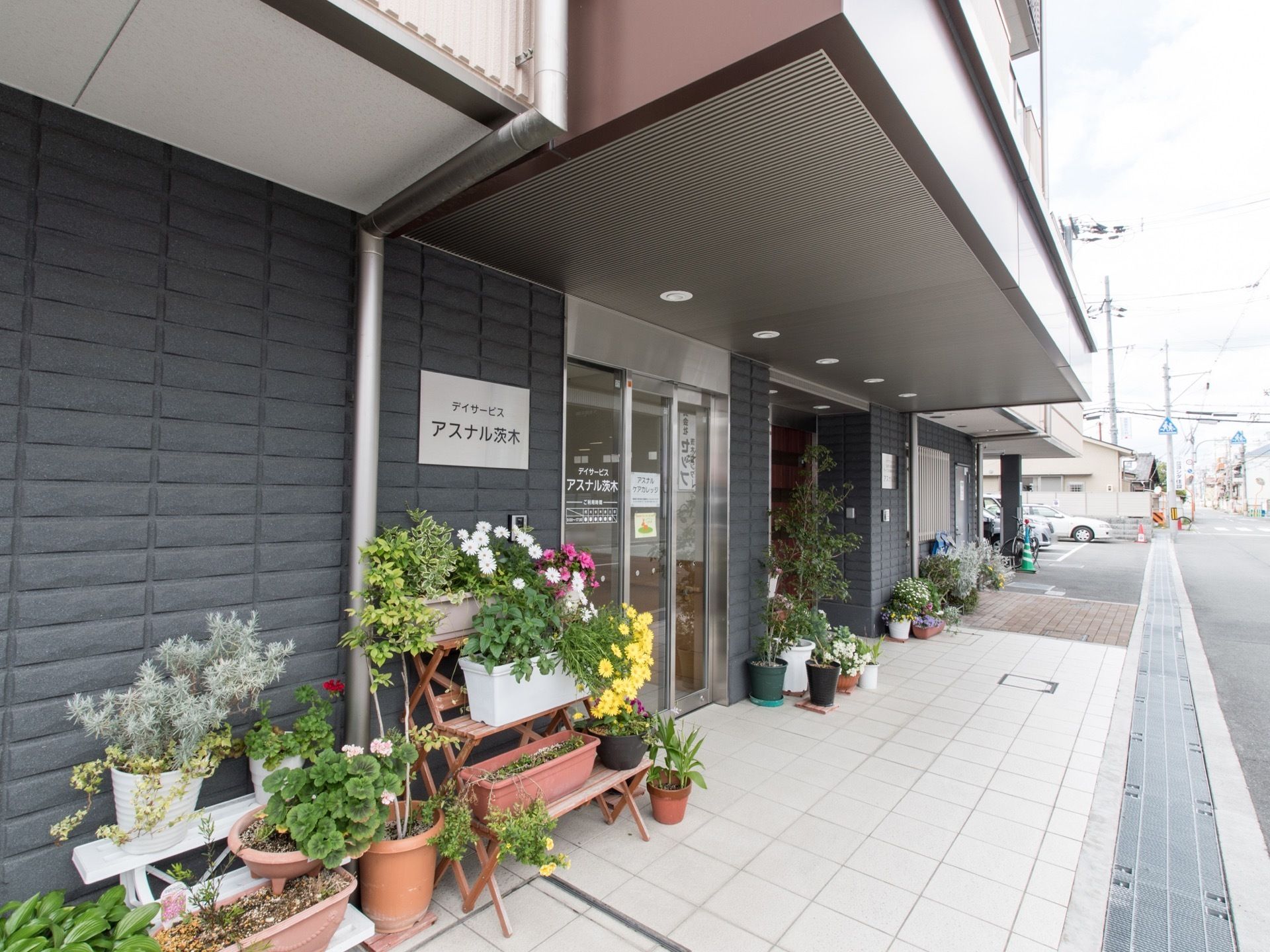 玄関には大きな屋根がついている。草花がたくさん置かれている。自動扉になっており、段差もなく、目の前は道路である。