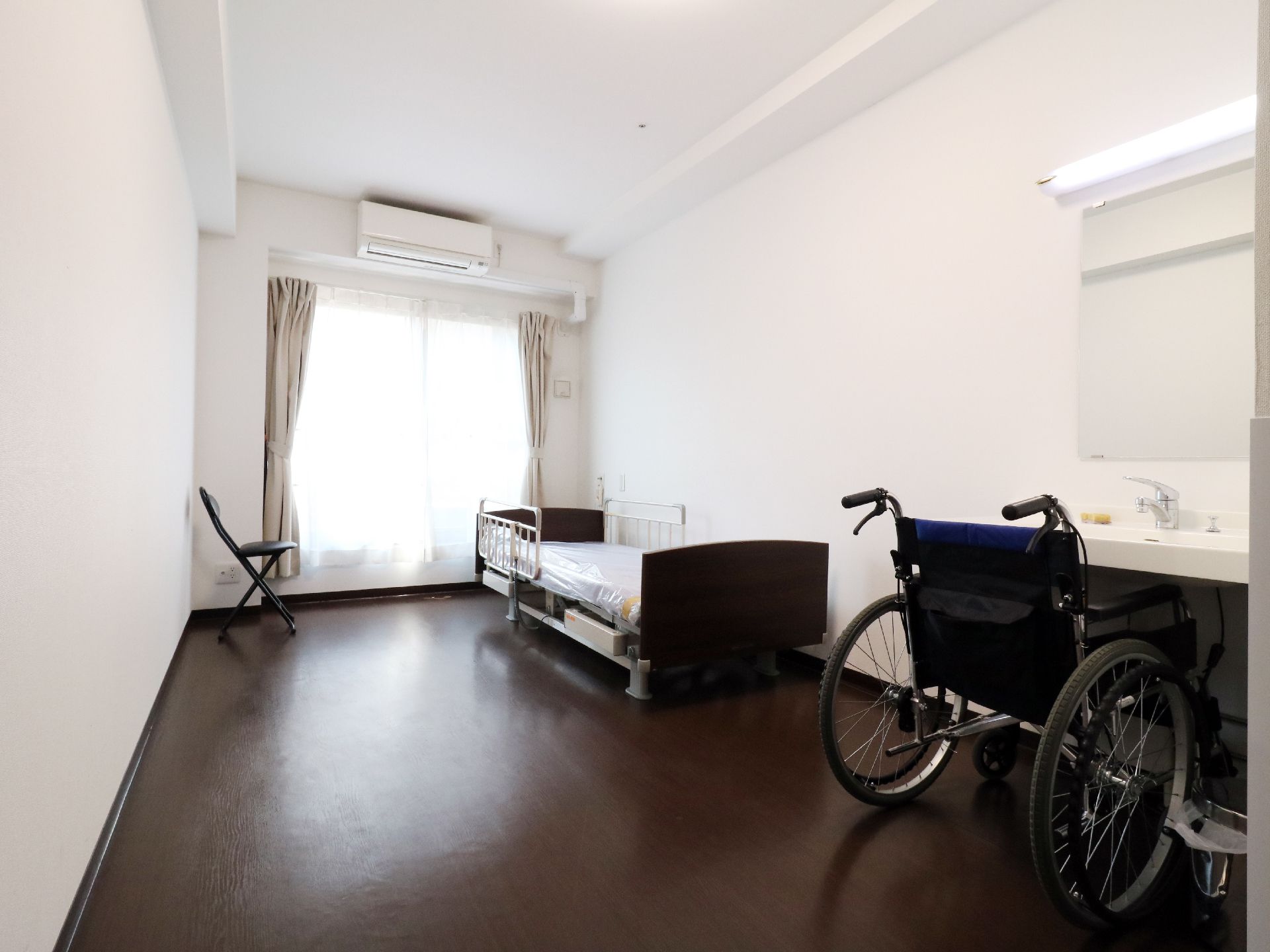 全室エアコン、洗面台、ベッド、トイレ完備。大きな窓がある。床やベッドフレームは落ち着いた色を使用している。