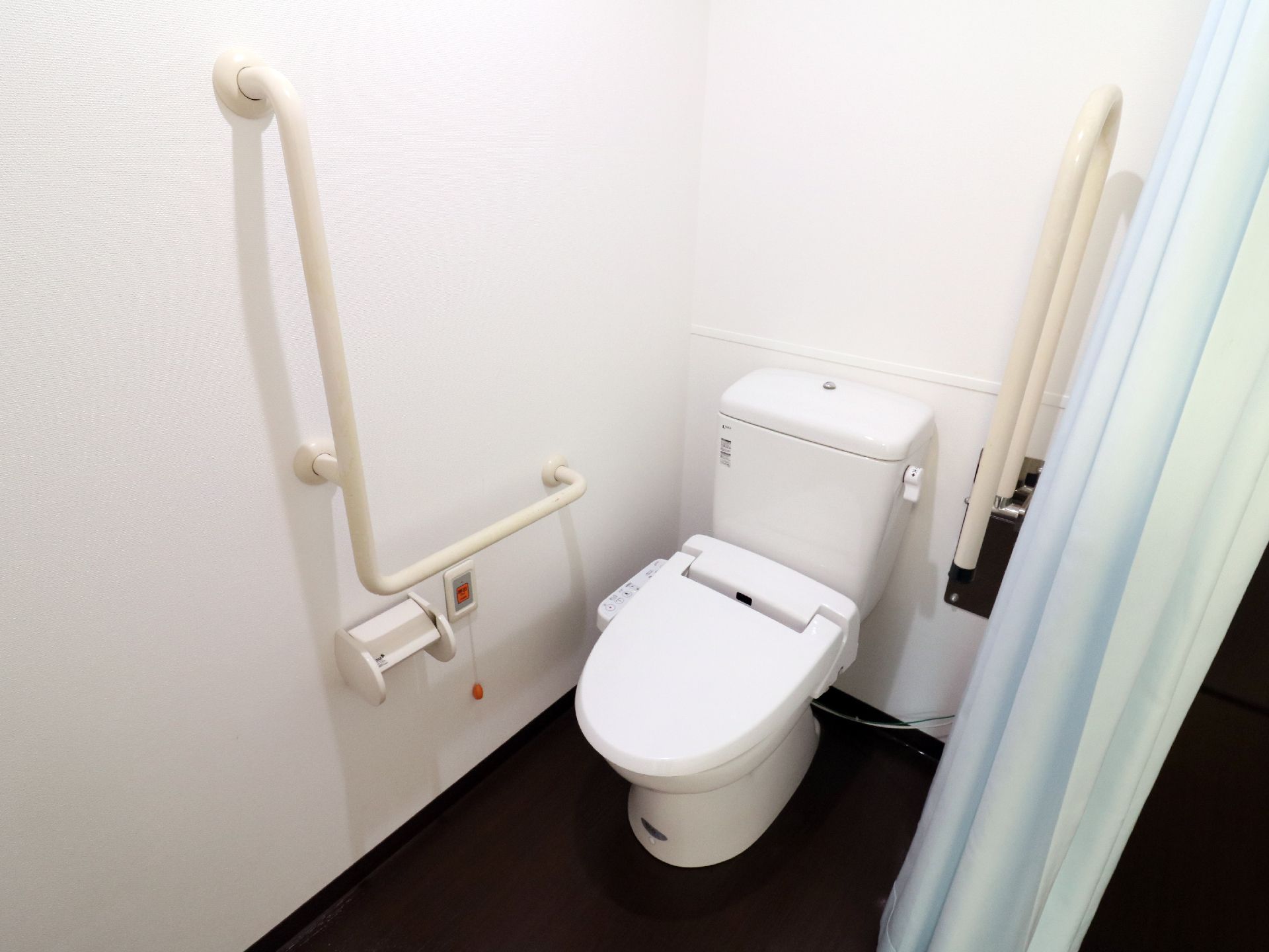 部屋とカーテンで仕切られた居室用のトイレ。全室シャワートイレを完備し、手すりやナースコールボタンも設置されている。