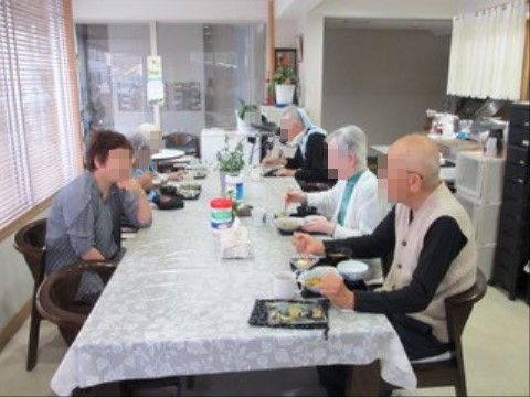 ダイニングルームで食事をする高齢者たちと、肘をついている女性