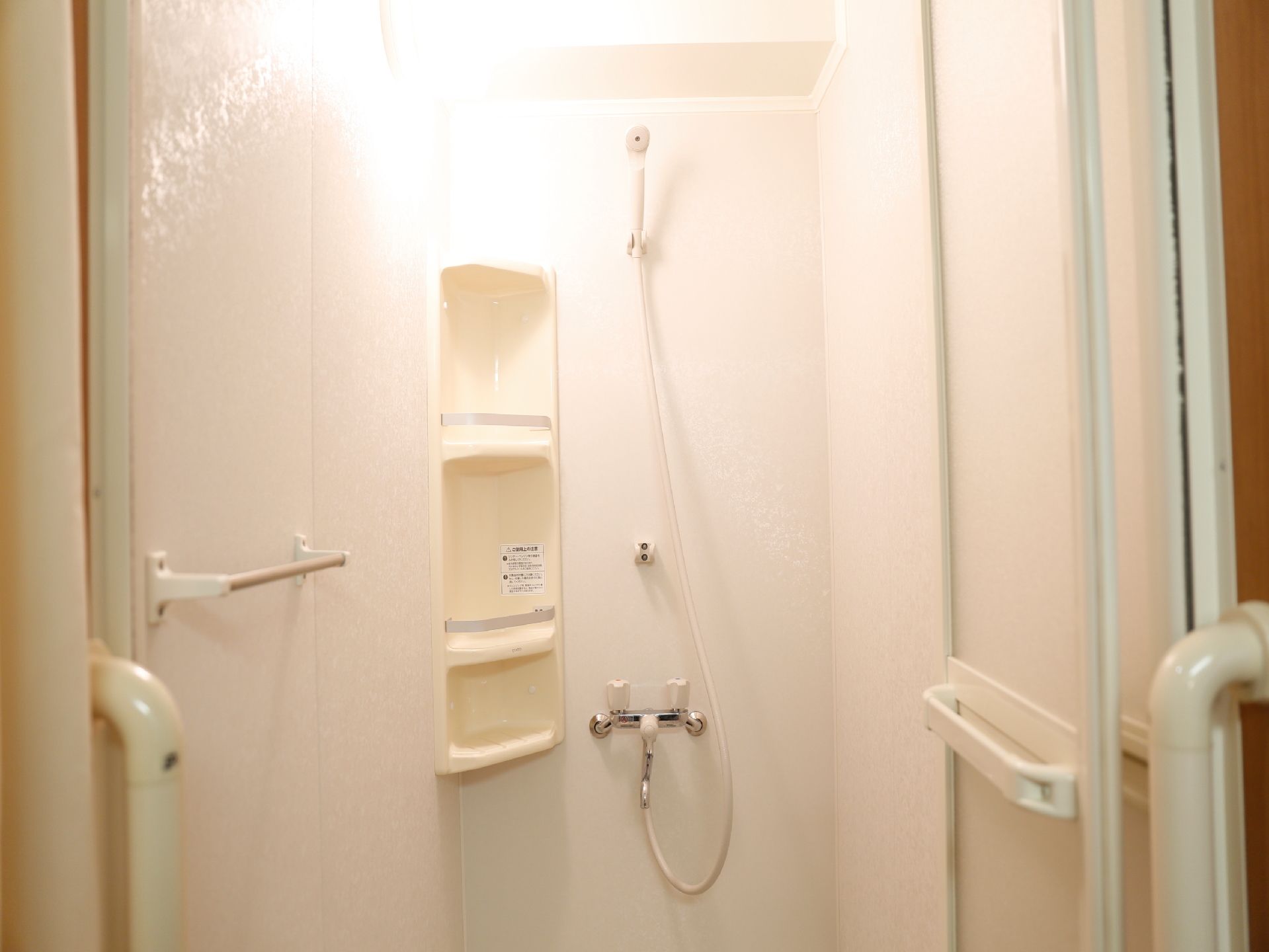 気軽に使用できる明るく清潔なシャワー室。手すり、収納ポケット、タオル掛けがコンパクトに設置されている。