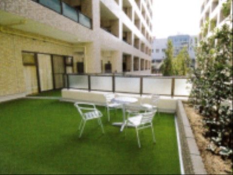 テラスには人口芝生が敷かれている。上には白いテーブルと椅子が用意されている。植え込みには緑の葉っぱが生えている。