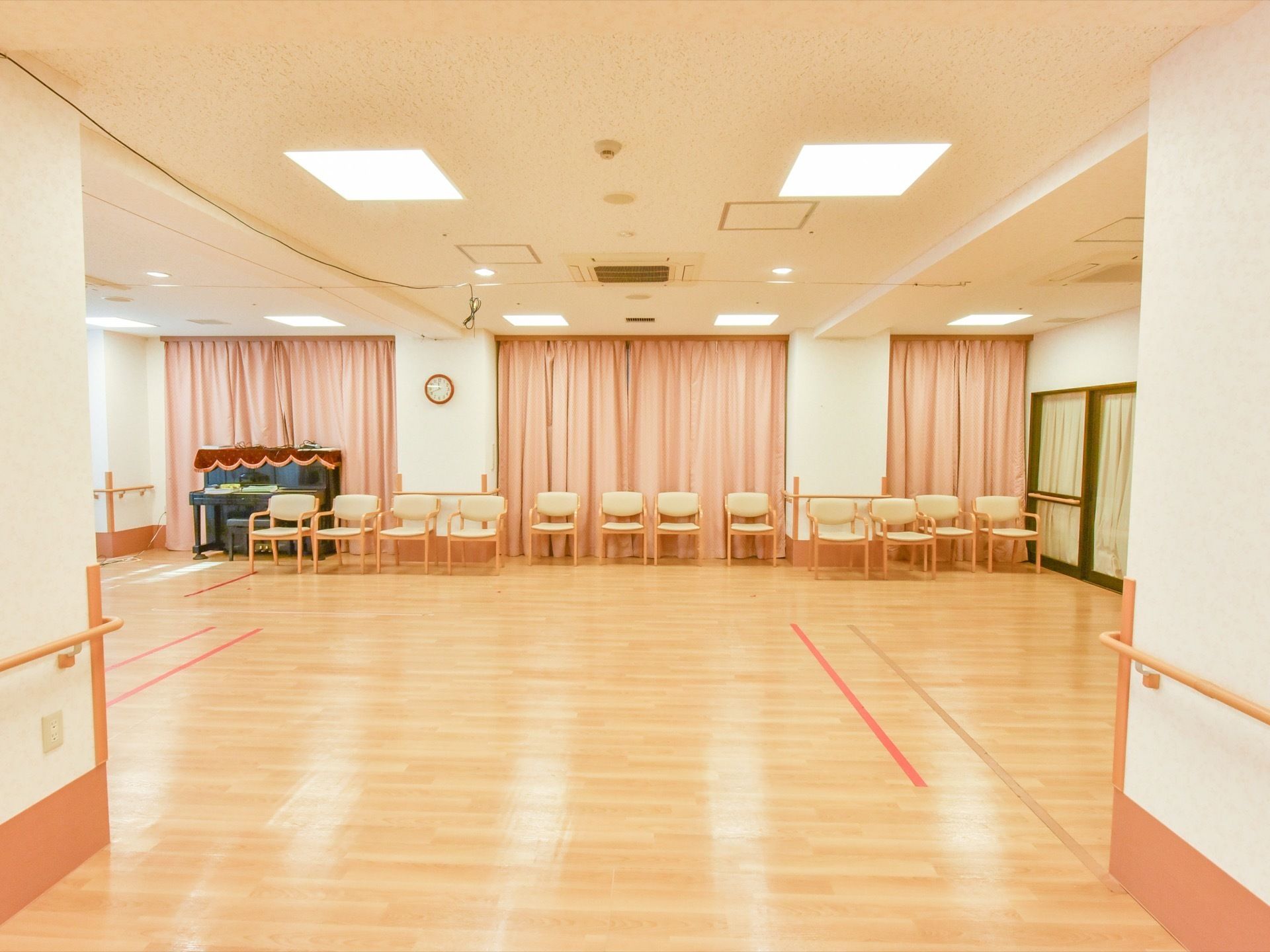 体育館のような広々とした共有スペース。椅子が数脚とピアノが置かれている。壁には手すりが設置されている。