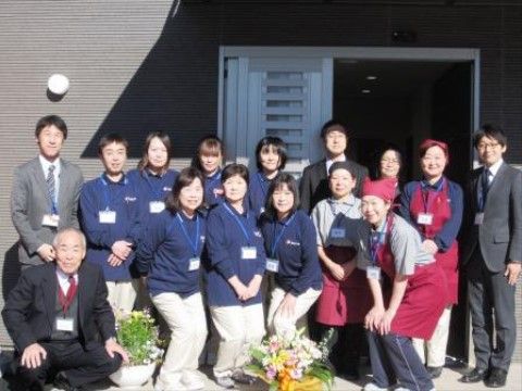 スーツやエプロン、シャツを身につけた施設職員たちの集合写真