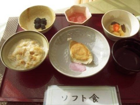 入居者様の好みや健康状態に応じて、柔らかく食べやすい食材を使用したメニューになっている。お盆の上にメニュープレートが置かれている。