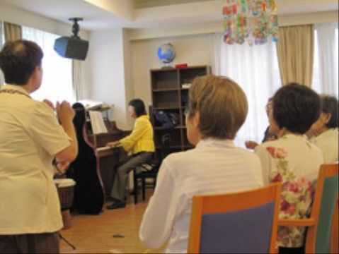 職員が弾くピアノに合わせて歌う椅子に座った高齢者たち