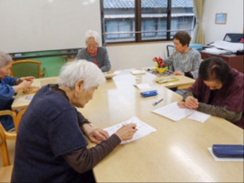 テーブルの席につき、真剣な面持ちで紙に何かを書く高齢者たち